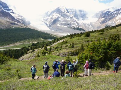 Group of Ramble Worldwide walkers pausing on mountainside dirt path to admire view of  snow-covered mountains, Canada