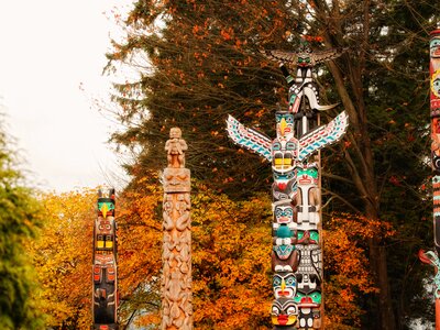 Totem poles with orange leaf deciduous trees surrounding nearby, Stanley Park in autumn, Vancouver, Canada